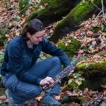 A scientist observes some woody material in a creek bed
